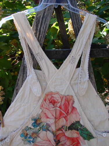 The Magnolia Pearl Applique Benjamin Overall Birdie Bouquet Moon OSFA features a quilted apron-style design with large pink roses, blue flowers, and vintage-inspired cross-back straps, reflecting a handcrafted aesthetic.