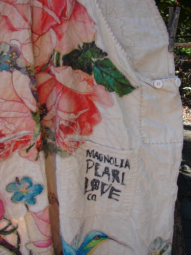 Magnolia Pearl Applique Benjamin Overall Birdie Bouquet Moon OSFA features quilted cream fabric with pink roses, green leaves, and a hummingbird. Visible pocket displays Magnolia Pearl Love Co. label.