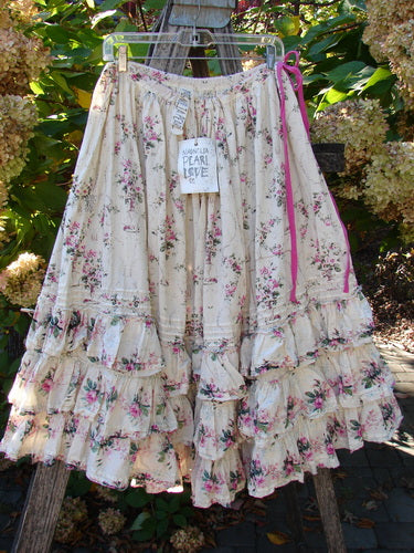 Magnolia Pearl Penelope Skirt Des Rosiers Floral Idealist OSFA displayed on a wooden ladder, featuring vintage-style floral print, tiered ruffles, pink ribbon waist, and signature patches, embodying romantic, creative elegance.