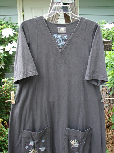 2000 Nova Dress Star Flower Orbit Size 0: Grey dress with flower design, reverse triangular neckline, wide sleeves, giant side drop pockets, and double vertical drawcord accents, displayed on a wooden rack.