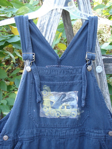 1996 Denim Overall Jumper Truck Travel Black Size 1, featuring a painted front bib pocket and sturdy metal buckle straps, displayed on a hanger in a garden setting with a wooden ladder.