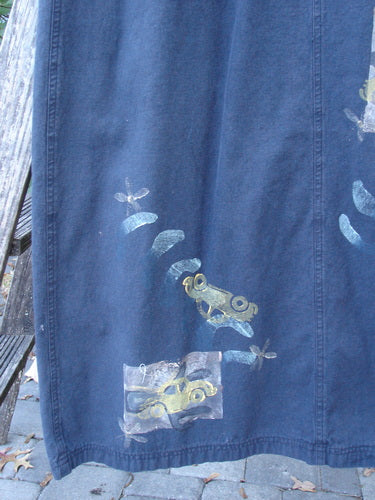 1996 Denim Overall Jumper Truck Travel Black Size 1 displayed outdoors, featuring stylized frog and leaf prints along the hem. It hangs over a wooden bench, showcasing the sturdy adjustable shoulder straps and painted front bib pocket.