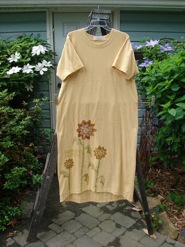 1998 Botanicals Calla Dress Tall Sunflower Sundial Dress Size 1 hanging on a wooden frame, showcasing a softly folded neckline, drop shoulders, and a sweet upward scooped hemline with sunflower prints.