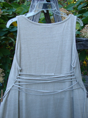 1998 Linen Knit Wrap Dress Unpainted Natural Size 2, featuring a sleeveless design with a rounded neckline and self-fabric ties across the lower back, elegantly displayed against green foliage and a wooden backdrop.