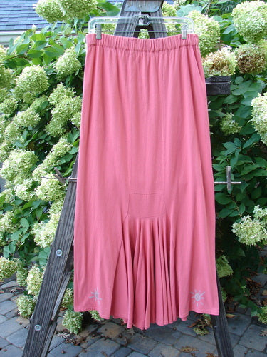 A 1995 Kick Pleat Skirt in Papaya, featuring a pink skirt on a wooden rack. Full elastic waist, elongating shape, rear kick pleat, and painted accents on the waistband. Perfect condition, made from organic cotton. Size 2.