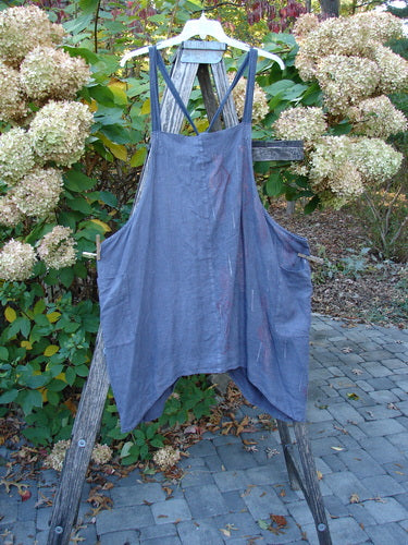 Barclay Linen Apron Jumper Celtic Rain Raven Size 2, displayed outdoors on a wooden ladder, features adjustable striped shoulder straps, banded upper bib, and two wrap drop side pockets.