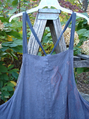 Barclay Linen Apron Jumper Celtic Rain Raven Size 2 displayed on a hanger against a wooden ladder. Features include a banded bib, adjustable striped straps, and two wrap drop side pockets.