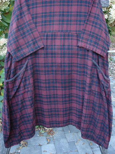 Barclay Flannel Bottom Bell Pocket Dress Merlo Plaid Size 2 hangs outdoors, showcasing its loose-fitting, smock-style design with wide three-quarter sleeves and large pockets in a warming plaid pattern.