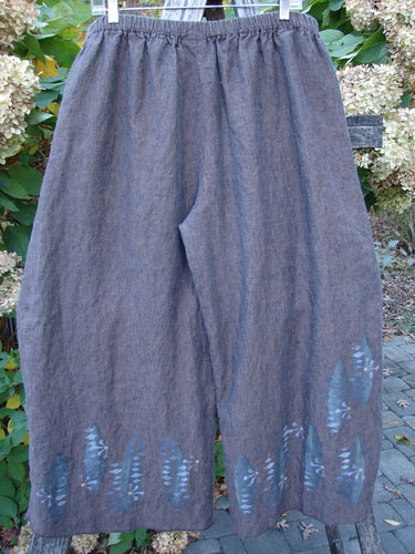 Barclay Cross Dye Linen Wide Leg Crop Pant Floral Sphere Wood Size 2, features loose-fitting, ankle-length design with a grayish fabric and blue leaf print along the hems, hanging outdoors on a clothesline.