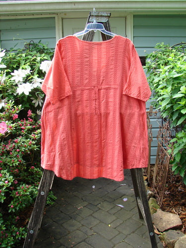 Barclay Linen Cotton Basket Weave Draw Back Tunic Unpainted Sherbert Size 2, short sleeved, displayed on a hanger outdoors.