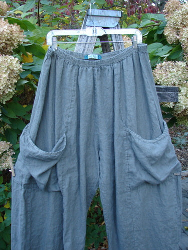 Barclay Lightweight Linen Side Pocket Pant Unpainted Army Stone Size 2, featuring a loose fit with drop-crotch design, elastic waistband, and oversized hip pockets, displayed on a hanger amidst a natural background.