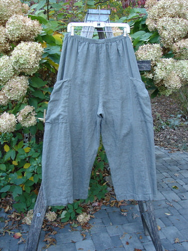 Barclay Lightweight Linen Side Pocket Pant Unpainted Army Stone Size 2, featuring an elastic waistband and roomy side patch pockets, hang on a ladder, showcasing their loose-fitting, cropped silhouette.
