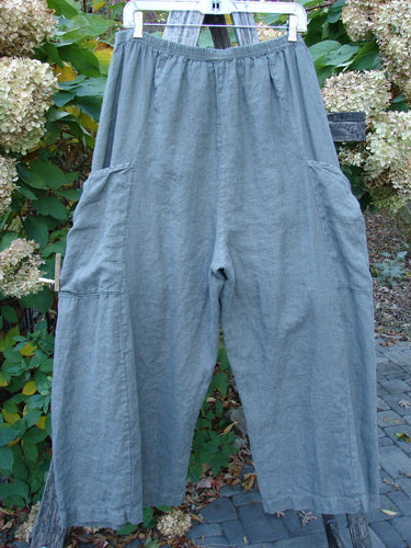Barclay Lightweight Linen Side Pocket Pant Unpainted Army Stone Size 2, featuring a loose fit, elastic waistband, and large hip pockets, hangs against a garden backdrop, epitomizing effortless summer style.