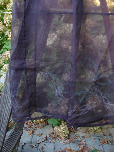 2000 Silk Organza Skirt Wind Whisp Aubergine Size 1: Sheer dark-blue skirt with faint floral embroidery, featuring a full elastic waist, vertical panels, and Celtic wind motifs, displayed in a garden setting.