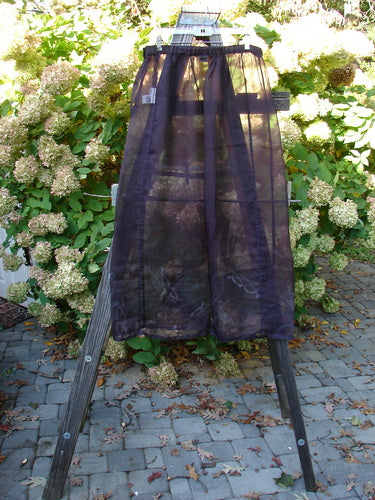 2000 Silk Organza Skirt Wind Whisp Aubergine Size 1 features a flowing A-line with Celtic wind patterns, displayed gracefully on a stone patio amidst hydrangeas, embodying vintage elegance from Bluefishfinder.com.