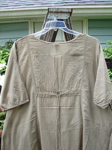 Barclay Batiste Bliss Dress Fallen Petal Stonetail Size 0 on a hanger, showcasing its soft rounded neckline, short sleeves, full center art section, exterior flop pockets, and drawcord back.