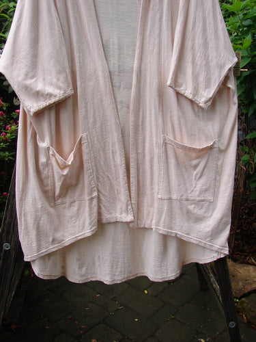 Barclay NWT Art Kimono Wind Dust Hush Pink Slub OSFA displayed on a clothes rack, showcasing its elegant dolman sleeves and flowing design.