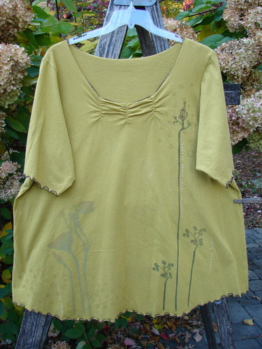 Barclay Gather Twinkle Top Berry Rise Yellow Olive Size 2, featuring elbow-length sleeves with lettuce-edge hems, a scooped neckline with gather detail, and a botanical print near the hem, displayed on a garden ladder.