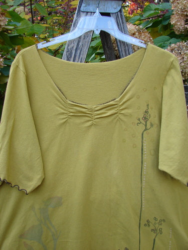 Barclay Gather Twinkle Top Berry Rise Yellow Olive Size 2, featuring a scooped neckline with center ruching, vine motif, and curly edgings, showcased on a hanger against a rustic background.