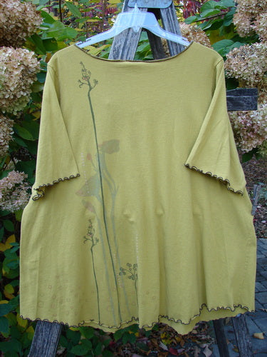 Barclay Gather Twinkle Top Berry Rise Yellow Olive Size 2: Loose-fitting, chartreuse tunic with elbow-length sleeves, ruffled trim, and botanical print, displayed outdoors on a wooden ladder amidst garden foliage.