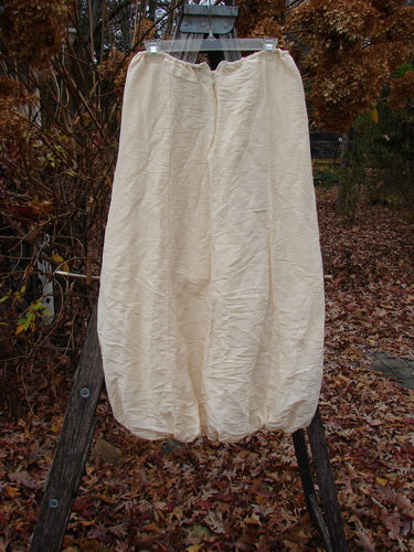 2000 Hemp Silk Reverse Skirt Unpainted Parchment Size 1 displayed on a wooden ladder, showcasing its loose, balloon-like silhouette with elastic ankles and a bubble hem, against an autumnal outdoor setting.