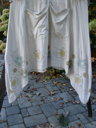 Barclay Cotton Lycra Double Pocket Bounce Tunic Dress Floral Creme Size 2, hanging on a clothesline, showcasing its festive floral garden theme with oversized front pockets and varying hemline.