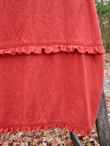 2000 Wool Pointelle Lulu Slip Dress Sienna Smaller Size 0, elegantly displayed with its distinctive criss-cross upper bodice and horizontal ruffled lower edge, draped over a wooden surface amongst autumn leaves.