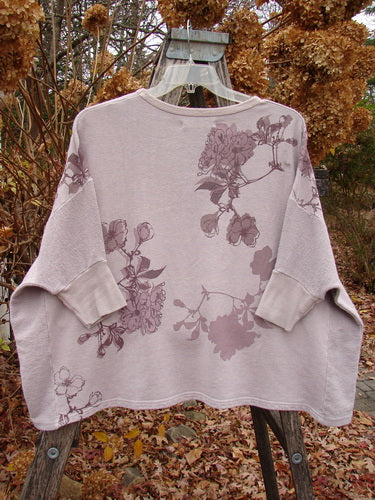 Barclay Colors Sweatshirt Dogwood Branch Pink Blush OSFA, featuring a loose boxy shape, floral motifs, banded sleeves, and contrasting side panels, displayed on a wooden ladder with an autumnal backdrop.