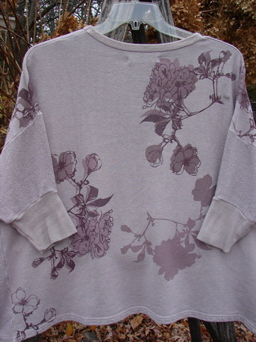 Barclay Colors Sweatshirt Dogwood Branch Pink Blush OSFA: A relaxed-fit, muted gray sweatshirt with a floral print, featuring a wide boxy shape, dolman sleeves, and contrasting textured side panels, hanging outdoors.