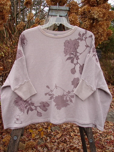 Barclay Colors Sweatshirt Dogwood Branch Pink Blush OSFA draped on a hanger, showcasing its wide, boxy shape, dolman banded sleeves, and floral theme amid dried hydrangeas and autumn leaves.