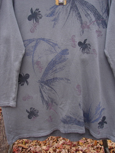 Barclay NWT Modal Organic Cotton Sketchbook Top Dragonfly Haze Size 1, featuring botanical motifs and fleur-de-lis patterns, hangs outdoors, showcasing its long sleeves, rounded neckline, and unique scooped hem.