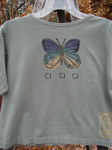 1996 Crop Tee Floral Butterfly Cricket Size 1 features a sage-green, short-sleeved, boxy tee with a stylized butterfly graphic and checkbox outlines, showcasing Blue Fish Clothing's vintage, artistic design ethos.