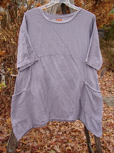 Barclay Gauze Two Pocket Urchin Dress in Light Plum Stripe, featuring elbow-length sleeves, scooped neckline, and hip-level patch pockets, displayed on a hanger with a wooden backdrop.