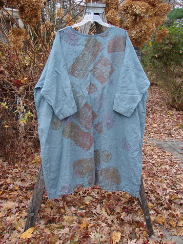 Barclay Linen Oversized Gallery Dress Falling Daisy Delaware OSFA, a mid-length tunic with a floral motif, displayed outdoors. Features include a rounded neckline, dolman sleeves, and a wide, pocketless design.