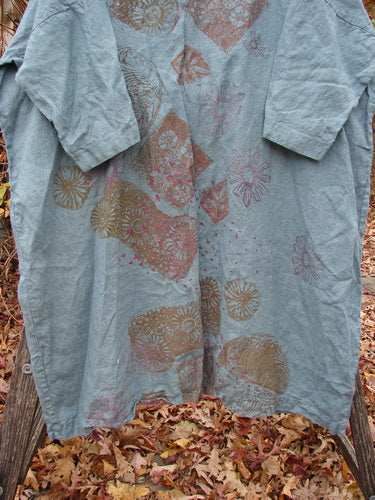 Barclay Linen Oversized Gallery Dress Falling Daisy Delaware OSFA draped on a wooden bench, showcasing its loose, knee-length design with three-quarter sleeves and hand-printed floral and geometric motifs on light blue linen.