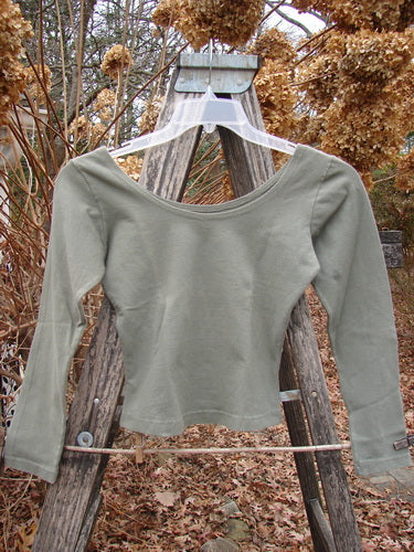 1994 Cotton Lycra Ballerina Layering Top Unpainted Seaweed Smaller Size 1 with a scoop neckline and long sleeves, displayed on a hanger against a rustic outdoor backdrop, highlighting its fitted design.