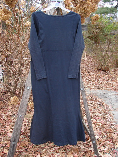 1992 Pedestal Dress Unpainted Black Size 1 features a modest rounded neckline, empire waist seam, and fishtail flares, displayed on a wooden ladder against an autumn backdrop, embodying vintage Blue Fish Clothing elegance.