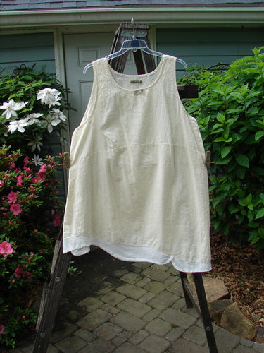 Barclay NWT Hemp Cotton Empire Flutter Pinafore Unpainted Creme Size 2, featuring a rounded neckline, asymmetrical hemline, and scallop flutter, displayed on a rack.