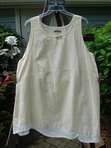 Barclay NWT Hemp Cotton Empire Flutter Pinafore in Creme, displayed on a clothes rack, highlighting its softly textured linen-like appearance and unique asymmetrical hemline with overlapping white scallop flutter. Size 2.