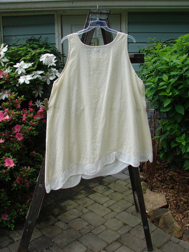 Barclay NWT Hemp Cotton Empire Flutter Pinafore in Creme on a hanger, showcasing its rounded neckline, asymmetrical hemline, and overlapping scallop flutter detail, perfect for a summer collection.