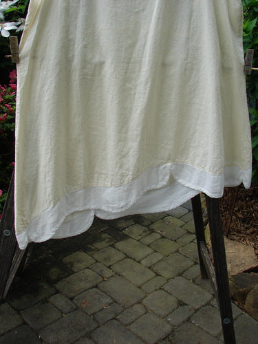 Barclay NWT Hemp Cotton Empire Flutter Pinafore Unpainted Creme Size 2 on a clothesline, showcasing its asymmetrical hemline, scallop flutter, and sweetly rounded neckline.