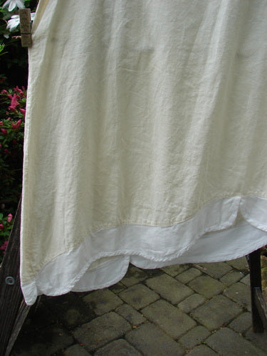 Barclay NWT Hemp Cotton Empire Flutter Pinafore Unpainted Creme Size 2 hanging on a clothesline, showcasing its rounded neckline, asymmetrical hemline, and softly textured linen-like fabric.