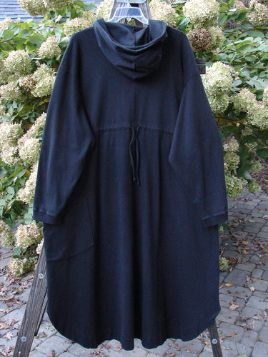 Barclay Interlock Hooded Dahlia Coat Unpainted Black OSFA displayed outdoors, showcasing its large cozy hood, unique hemline, and oversized pocket, reflecting BlueFishFinder's vintage and creative clothing ethos.