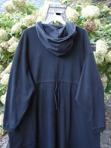 Barclay Interlock Hooded Dahlia Coat Unpainted Black OSFA displayed on a hanger, featuring an oversized hood, front and rear hemline, ribbed cuffs, and a deep exterior pocket with recycled buttons.