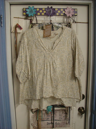 Magnolia Pearl NWT European Cotton Bondi Blouse Fleuri OSFA, featuring a light, loose-fit design with subtle paisley prints, raw-edged V-neckline, and pintuck accents, displayed on a decorative wall rack.