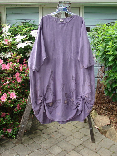 Barclay Hemp Cotton Silk Voile Belle Dress in Violet, displayed on a clothes rack, showcasing its artistic wing and flower theme paint, wide neckline, and unique bell shape design.