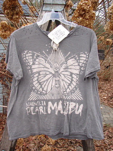 Magnolia Pearl NWT Cotton Jersey Boyfriend Tee MP Malibu Ozzy OSFA hangs on a rustic ladder, featuring a butterfly graphic with Magnolia Pearl Malibu text, showcasing a drapey, distressed, and uniquely shaped design.