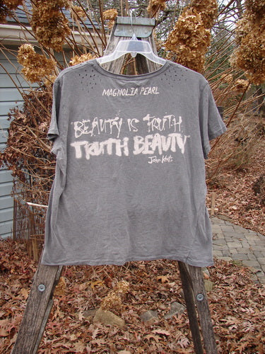 Magnolia Pearl NWT Cotton Jersey Boyfriend Tee MP Malibu Ozzy OSFA hangs on a wooden A-frame, showcasing white lettering of John Keats' quote on its heather-gray fabric, embodying artistic individuality.