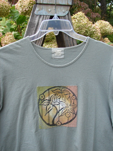 1999 Patched Short Sleeved Crop Tee Tri Floral Shale Size 2 displayed on a hanger, showcasing the classic tri-floral patch design and thin rolled neckline, highlighting its vintage appeal and organic cotton fabric.
