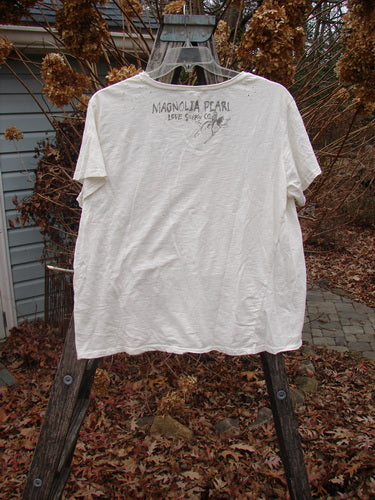 Magnolia Pearl Cotton Jersey Short Sleeved Boyfriend Tee True OSFA draped on a wooden ladder, showcasing its rolled edges, slight A-line shape, and diagonal wrap seam amidst an outdoor setting.